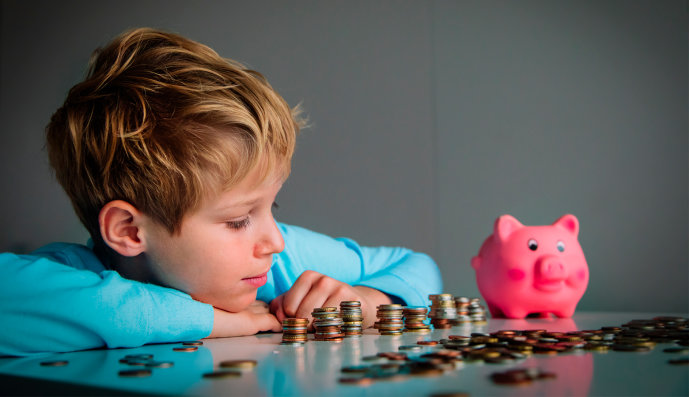 Foto:  Kleiner Junge sitzt am Tisch und zählt seine Münzen. Auf dem Tisch steht sein Sparschwein.