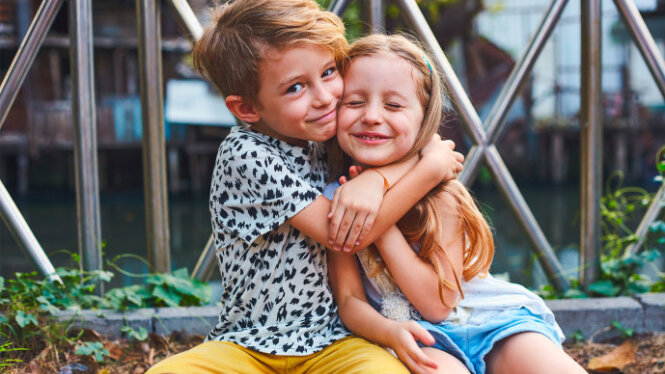 Foto: Junge und Mädchen umarmen sich und lachen in die Kamera.