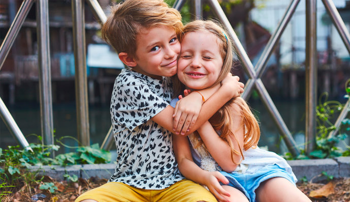 Foto: Junge und Mädchen umarmen sich und lachen in die Kamera.