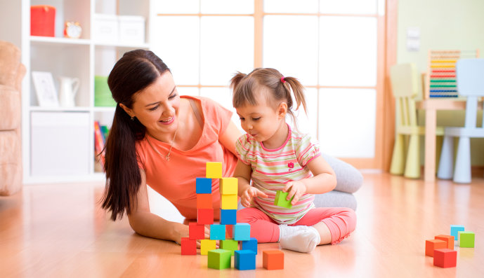 Foto: Mutter und Tochter sitzen auf dem Fußboden und bauen aus Spielzeugblöcken ein Haus.