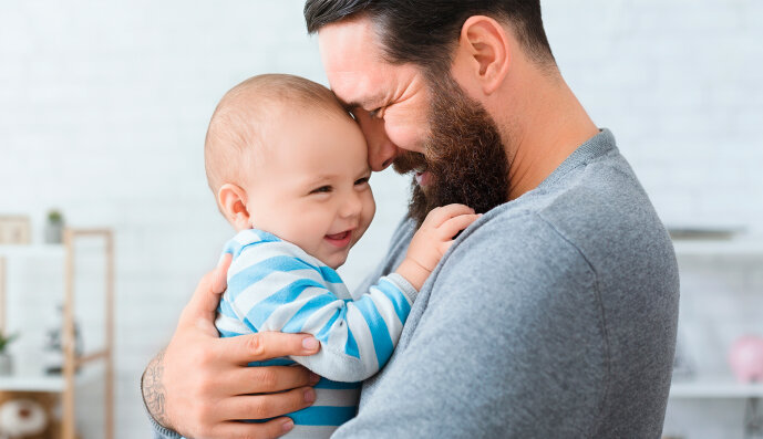 Foto: Fröhlicher Vater hält sein lachendes Baby umarmt.