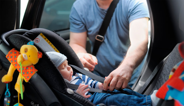 Foto: Vater schnallt sein Baby im Auto in der Kindersitzschale an.