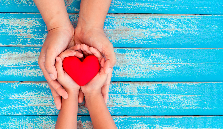 Foto: Eine Hand eines Erwachsenen und eine Kinderhand halten zusammen ein Herz