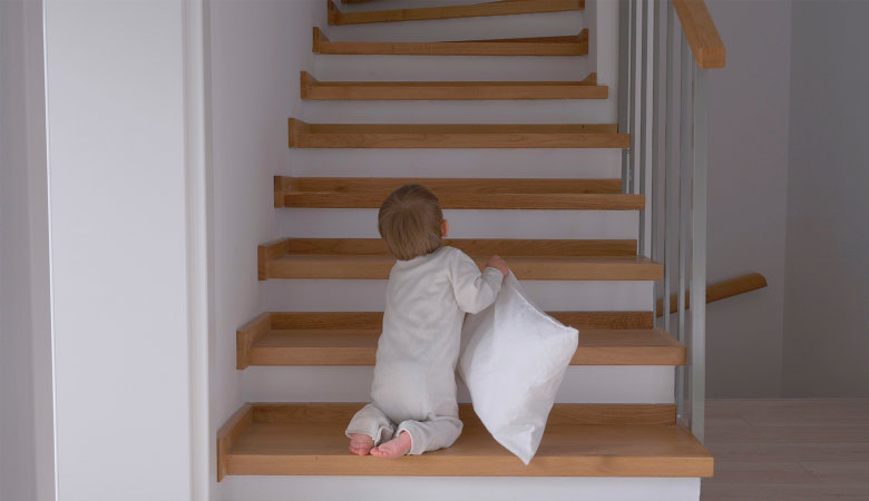 Foto: Kleines Baby mit Kissen in der Hand krabbelt die Treppe hoch.