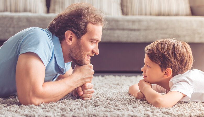 Foto: Seitenansicht von Vater und Sohn, die auf dem Teppich sich gegenüber liegen und sich ansehen.