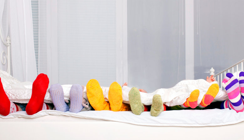 Foto: Sechs Paar Füße mit Socken schauen unter der Bettdecke hervor.