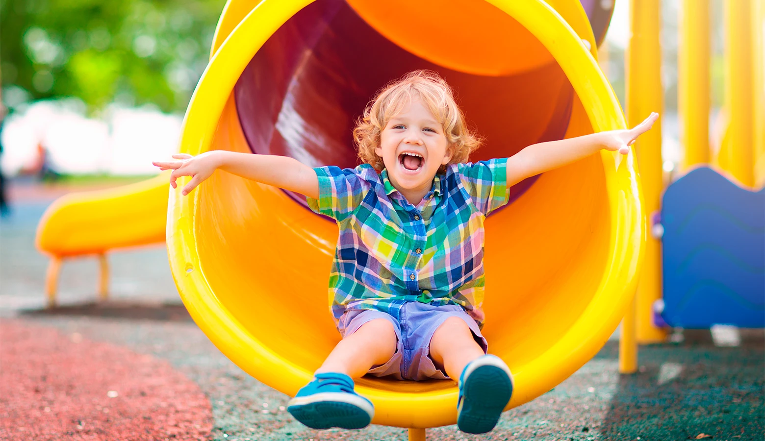 Foto: Fröhlicher kleiner Junge auf dem Spielplatz rutscht in einer Röhre.