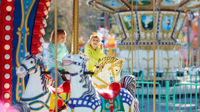 zwei Mädchen sitzen auf Pferden auf einem Karussell