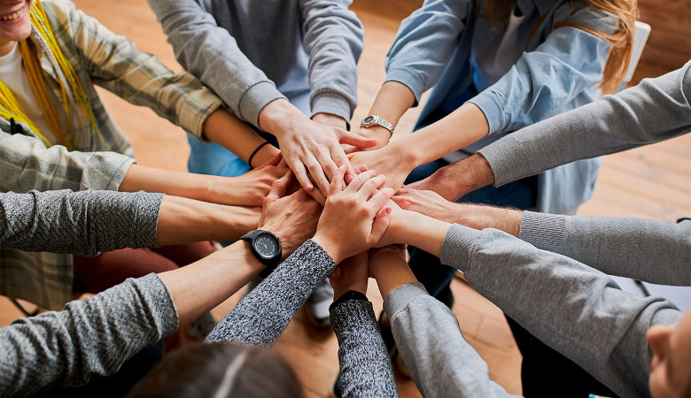 Foto: Sieben junge Personen stehen im Kreis und strecken ihre Hände in der Mitte zusammen