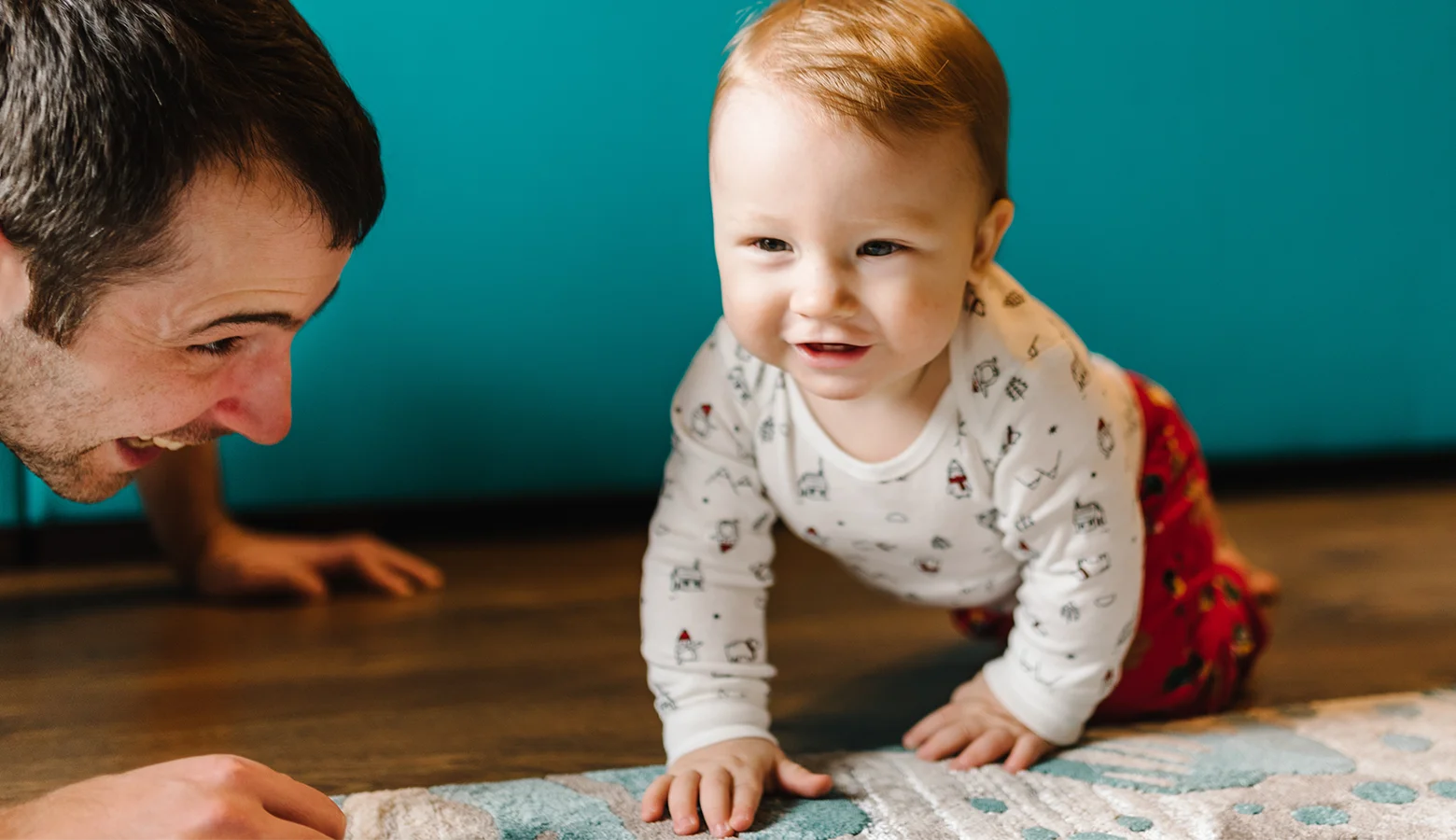 Lachender Papa sieht seinem Baby beim Krabbeln zu.