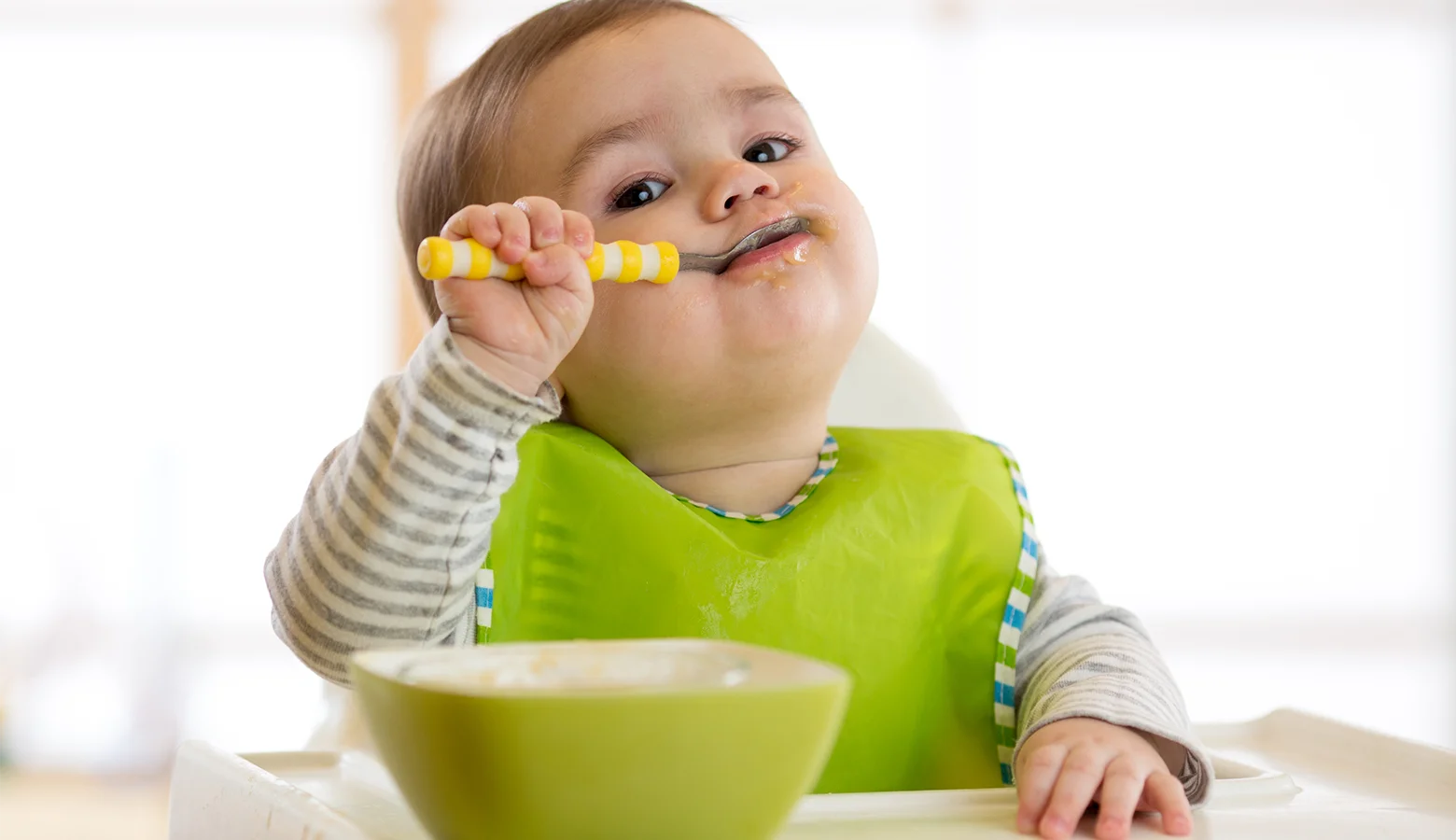 Baby sitzt im Kinderstuhl und löffelt einen Brei.