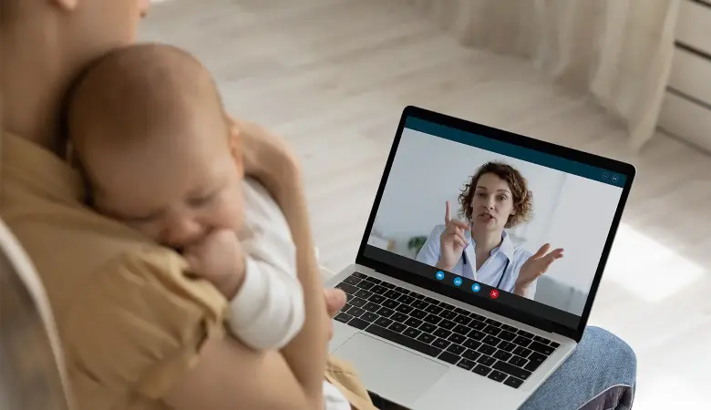 Mutter mit Baby auf dem Arm chattet mit Laptop mit einer Beraterin
