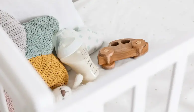 In einem Baby Kinderbett liegen Milchflasche und ein Holzspielzeug