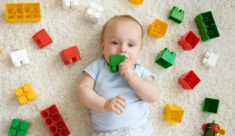 Baby liegt auf dem Teppich mit Legosteinen um sich rum