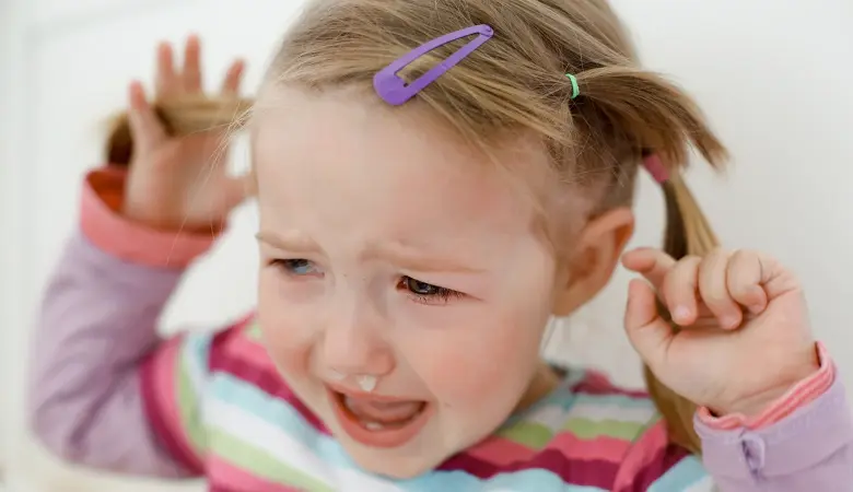 Ein Mädchen mit 2 Zöpfen und einer Haarspange weint, die Nase läuft