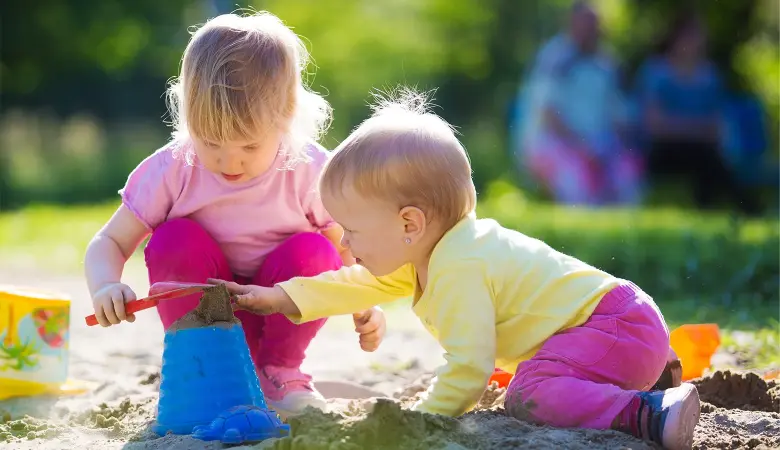Zwei Babys spielen mit Schaufel und Eimer in einem Sandkasten