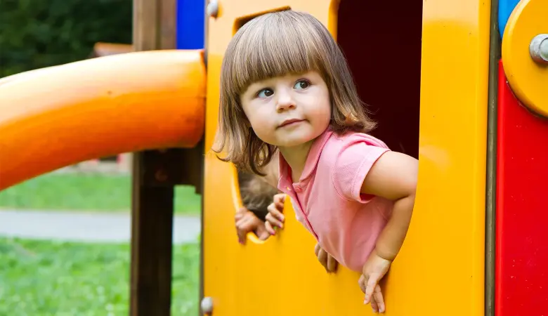 Ein Mädchen ist auf einem Spielplatz und schaut aus einem Spielhaus aus dem Fenster