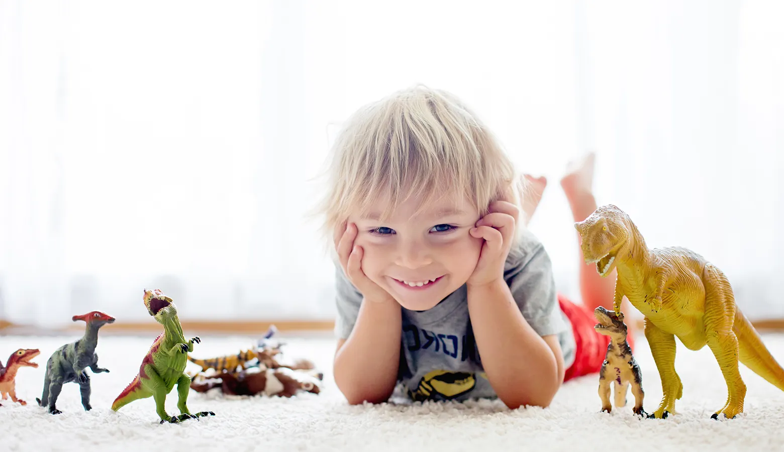 Ein Junge liegt auf dem Teppichboden um ihn herum sind Dinos aufgereiht