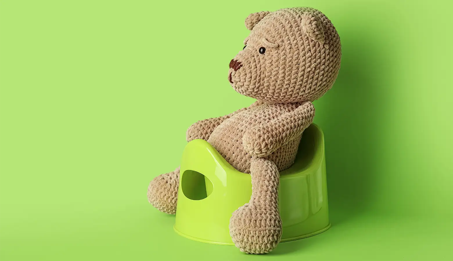 Ein gestrickter Teddybär sitz auf einem Kindertöpfchen