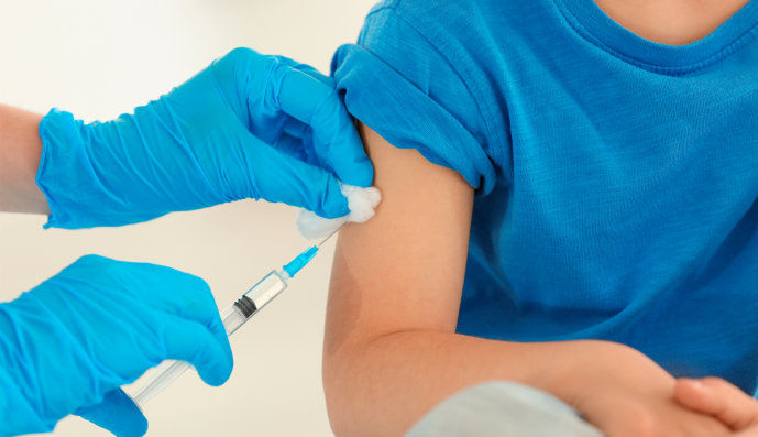 Foto: Ärztin mit Sicherheitshandschuhen hält eine Spritze in der Hand und impft ein Kind.