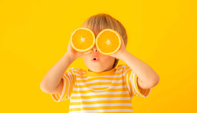 Foto: Fröhliches Kindergartenkind verdeckt die Augen mit zwei Orangenscheiben