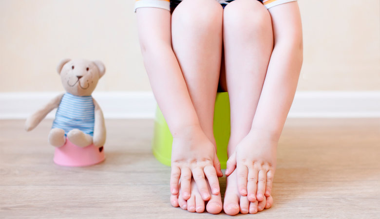 Foto: Nahaufnahme der Beine eines Kindes, das auf dem Töpfchen sitzt. 