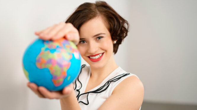 Foto: Lachende junge Frau hält einen Globus mit beiden Händen in die Kamera