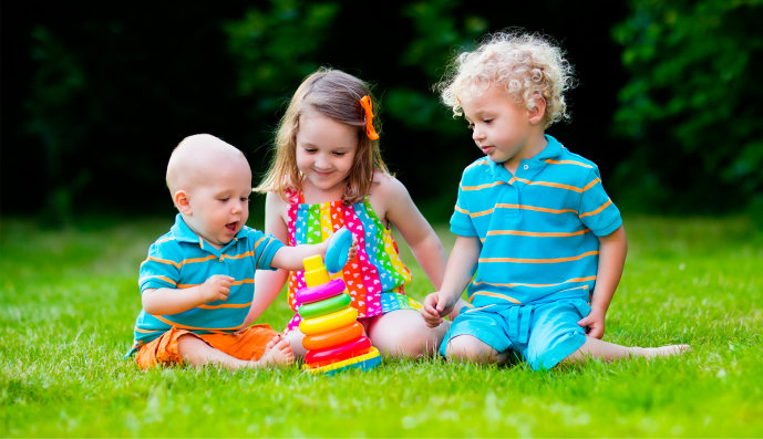 Foto: Drei kleine Kinder sitzen zusammen in der Wiese und spielen