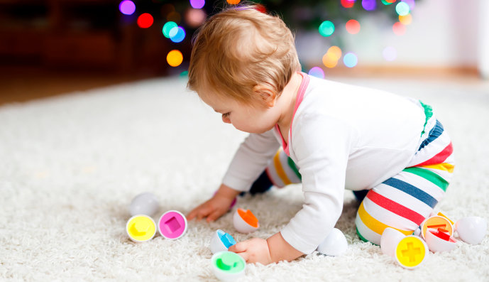 Foto: Baby, das auf dem Teppich mit Plastikspielzeug spielt