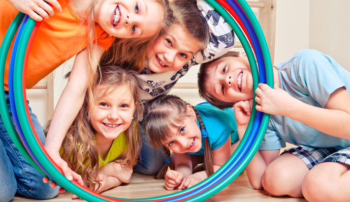 Foto: Fünf fröhliche Kinder, die durch einen Hula-Hoops Reifen schauen
