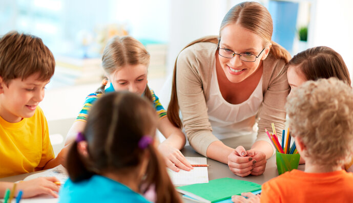 Foto: Kindergärtnerin sitzt mit fünf Kinder am Tisch und malt mit ihnen