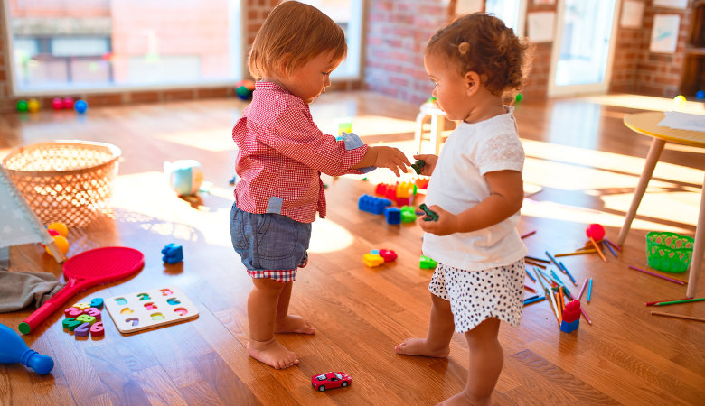 Foto: Zwei stehende kleine Mädchen, die in der Kinderkrippe spielen.
