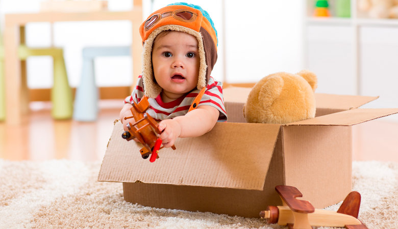 Foto: Kleiner Junge sitzt mit Mütze und Pilotenbrille in einem Pappkarton mit Spielsachen