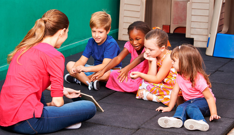 Foto: Gruppe von vier Kindern, die mit Kindergartenlehrerin in der Vorschule über ein Buch sprechen