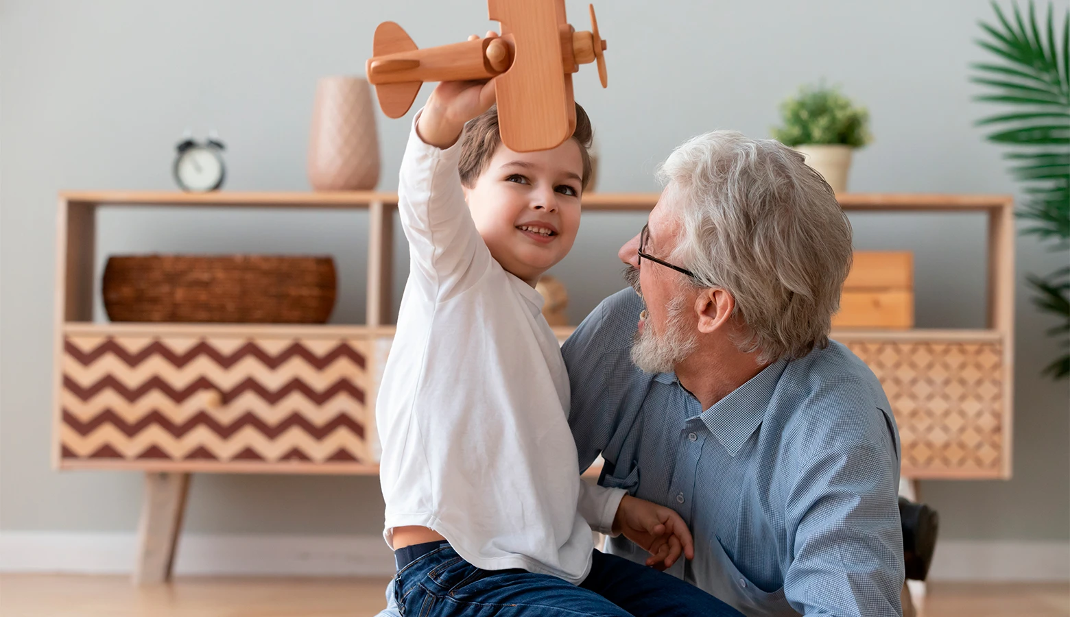 Foto: Fröhlicher Großvater hält seinen kleinen Enkel mit einem Holzflugzeug im Arm