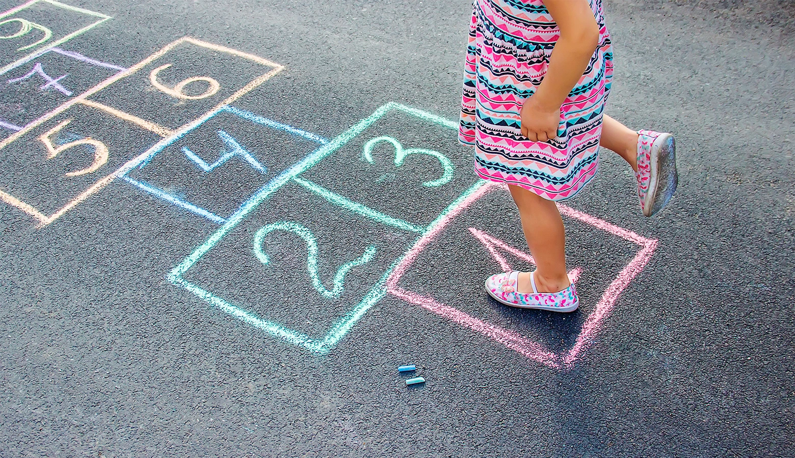 Foto: Ein Kind hüpft auf der Straße in Kreide bemalte und nummerierte Kästchen.