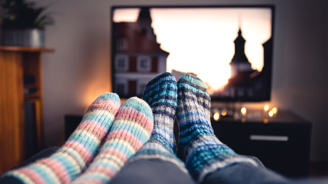 Foto: Zwei Paar Füße mit Wollsocken und ein Fernsehgerät im Hintergrund