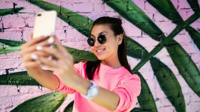 Mädchen mit Sonnenbrille macht mit dem Smartphone ein Selfi