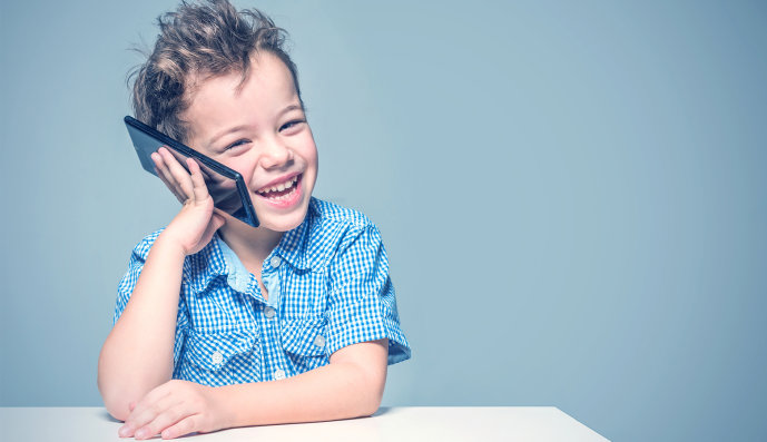 Foto: kleiner Junge hält lachend ein großes Smartphone an sein Ohr.