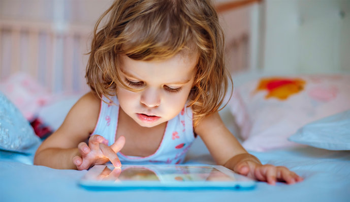 Foto: Zweijähriges Mädchen liegt auf dem Bett und spielt mit einem Tablet