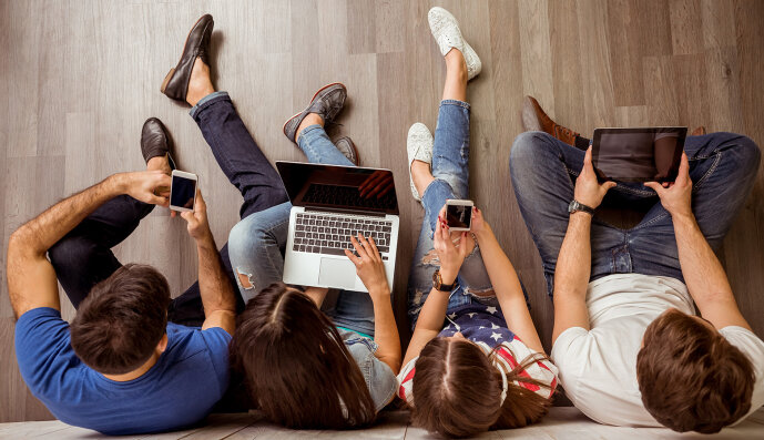 Gruppe Jugendlicher sitzt mit Smartphone, Tablet und Laptop am Fußboden