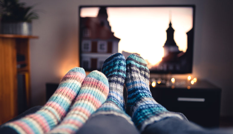 Foto: Zwei Paar Füße mit Wollsocken und ein Fernsehgerät im Hintergrund