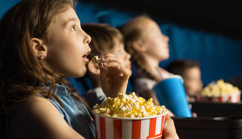 Foto: Staunendes Mädchen sitzt mit einer Popkorntüte im Kinosaal.