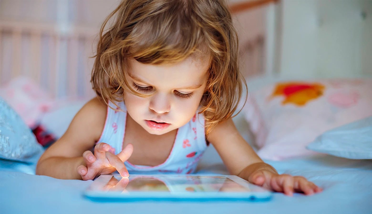 Foto: Kleinkind liegt auf dem Bett und spielt mit einem Tablet