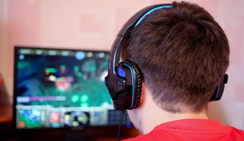 Junge mit Kopfhörer sitzt vor dem Bildschirm und spiel Computerspiel