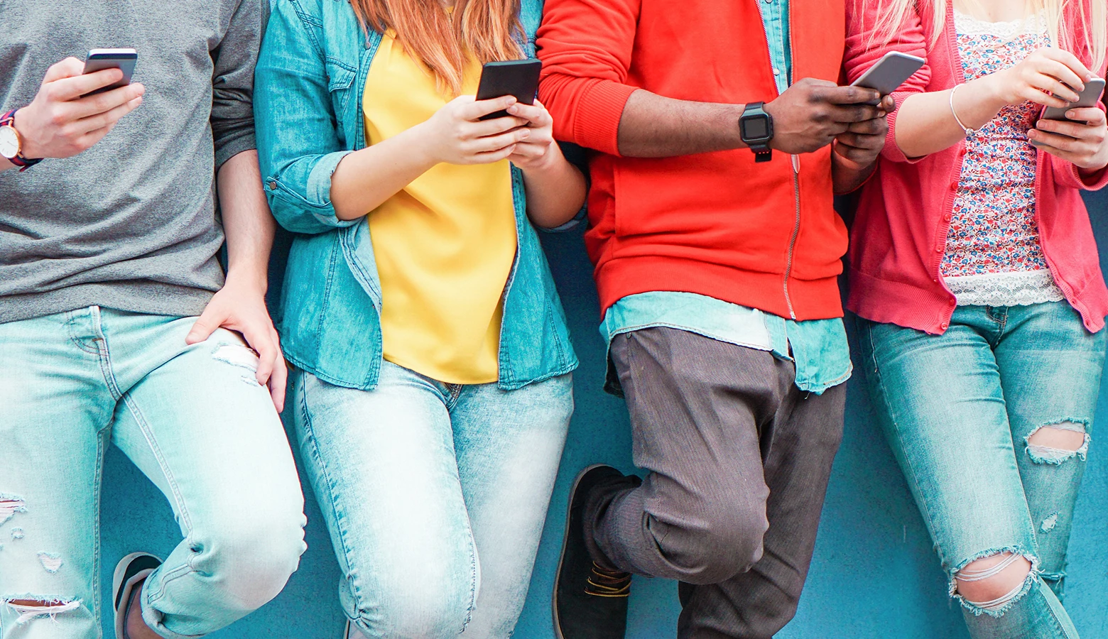 Foto: Vier Jugendliche mit ihren Smartphones stehen an eine Wand gelehnt.