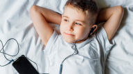 Foto: Junge liegt auf dem Bett und hört Musik mit Kopfhörer und Smartphone 