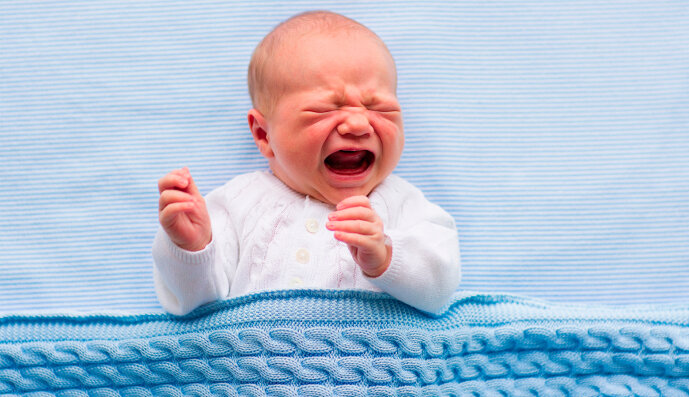 Foto: Baby-Junge, der schreiend und weinend in seinem Bettchen liegt.