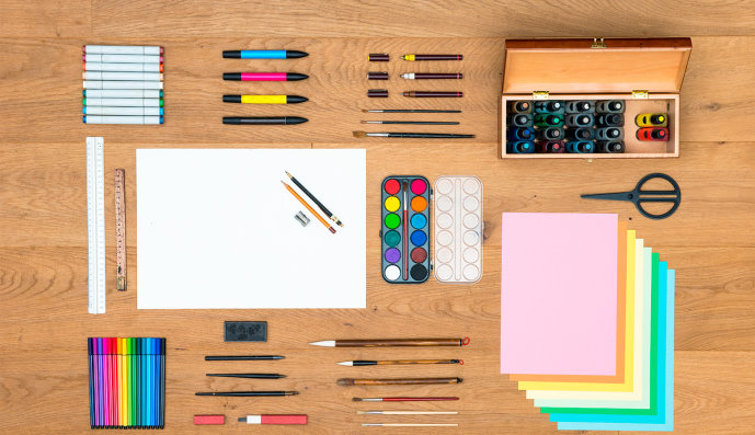 Foto: Stifte, Lineale, Marker, Pinsel mit Fontänen, Aquarellfarben und verschiedene Blätter liegen sehr ordentlich auf einem Schreibtisch.