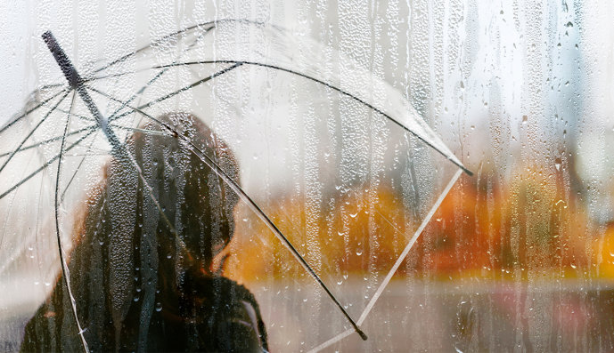 Foto: Silhouette eines jungen Mädchens, das mit einem Regenschirm im Regen steht.